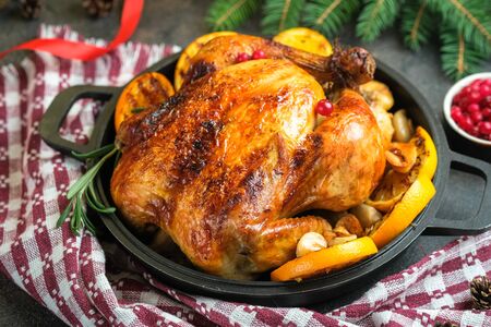 Christmas food. Roasted chicken with orange, cranberries, garlic and rosemary on a dark background. Festive table with Christmas decorations.の写真素材