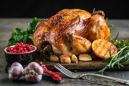 Christmas food. Roasted chicken with orange, cranberries, garlic and rosemary on a dark background. Festive table with Christmas decorations.の写真素材