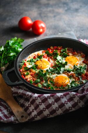Traditional  shakshuka with eggs, tomato, and parsley in a iron pan on a dark backgroundの写真素材