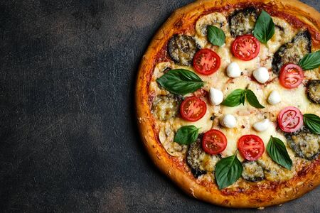 Traditional Italian pizza with eggplants, mozzarella, basil and tomatoes on a dark background top view copy space.の写真素材