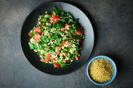 Traditional oriental salad Tabbouleh with bulgur and parsley on a dark background top view copy...