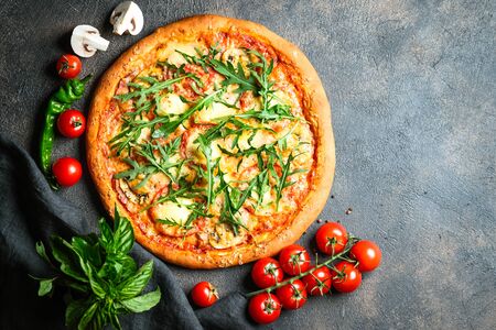 Traditional Italian pizza with ham, mozzarella, basil, arugula and tomatoes on a dark background top view copy space.の写真素材