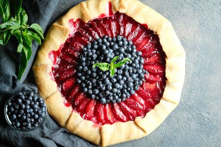Homemade backing. Delicious galette with plums and blueberries on a dark background copy space top viewの写真素材