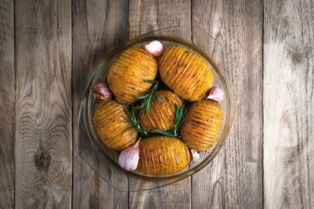 Baked potatoes with herbs and garlic in a round glass dish on a rustic background. Top view free...