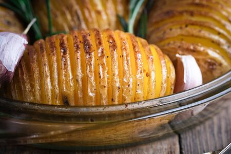 Baked potatoes with herbs and garlic in a round glass dish on a rustic background.