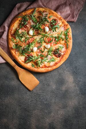 Traditional Italian pizza with ham, mushrooms, arugula, mozzarella, basil and tomatoes on a dark background top view copy space.の写真素材