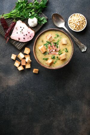 Pea soup with bacon, herbs and bread crumbs in rustic bowl on a dark background. Top view, copy space.の写真素材