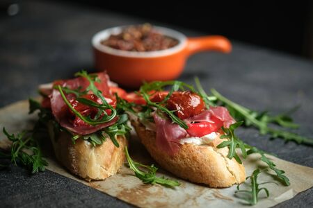 Traditional italian bruschetta with tomatoes, prosciutto, cream cheese and arugula on stone dish on a dark background with copy spaceの写真素材
