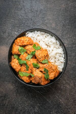 Chicken tikka masala traditional Asian spicy meat food with rice tomatoes and cilantro in a black bowl on dark background. Top view.の写真素材