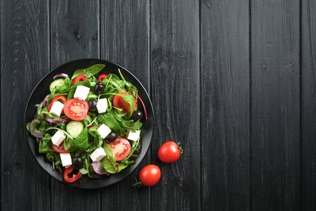 Fresh vegetable salad with feta, olives and herbs in a dark plate on a dark rustic background. Healthy vegan food. Top view copy space.の写真素材