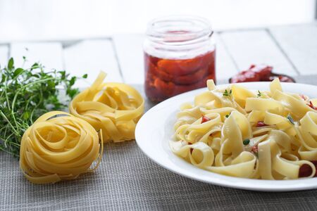 Italian traditional pasta tagliatelle with dried tomatoes and thyme on a light background.の写真素材