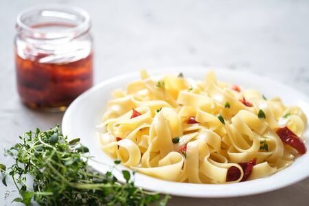 Italian traditional pasta tagliatelle with dried tomatoes and thyme on a light background.の写真素材