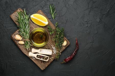Selected ingredients for cooking. Lemon, herbs, olive oil and spices on a cutting board on a dark...