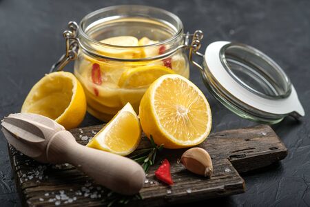 Salted lemons in glass jar with ingredients on a dark background. Moroccan cuisine.の写真素材