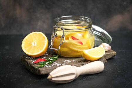Salted lemons in glass jar with ingredients on a dark background. Moroccan cuisine.