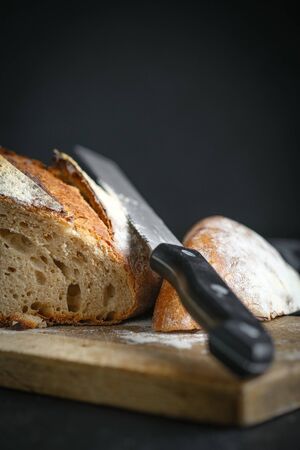 Bread. Homemade sliced whole grain bread on a cutting board with a knife on a dark background copy space.の写真素材