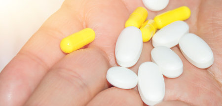 Open palm of a woman with a bunch of white and pink pills, health and medicine concept, close-up.の写真素材