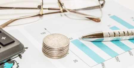 Concept of Finance and planning, coins, pen, glasses, calculator on the background of a table with business chartsの写真素材
