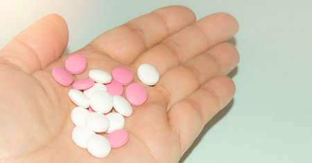 Open palm of a woman with a bunch of white and pink pills, health and medicine concept, close-upの写真素材
