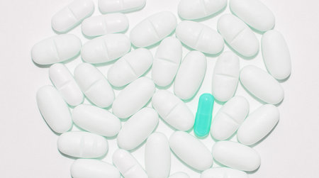 Scattered many white pills and one green pill on a white background, top viewの写真素材