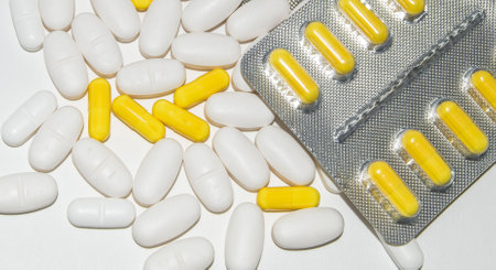 Silver blister packs of yellow pills and scattered white pills on a white background, top viewの写真素材