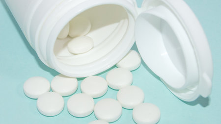 White open plastic jar with a bunch of white scattered pills on a light blue background, medicine concept, bannerの写真素材