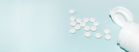 White open plastic jar with a bunch of white scattered pills on a light blue background, medicine concept, copy of the space, bannerの写真素材