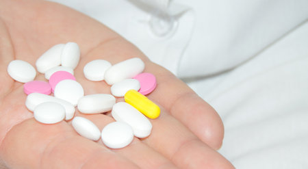 Open palm of a woman with a bunch of white and pink pills, health and medicine concept, close-upの写真素材