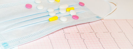 Medical mask and tablets on paper electrocardiogram, prevention of heart diseasesの写真素材