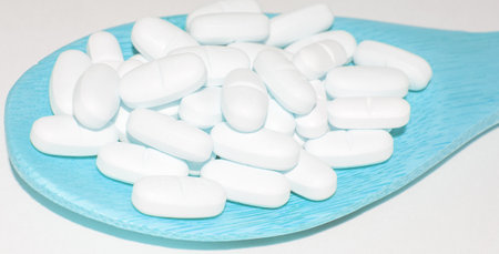 White tablets in a blue wooden spoon, isolated on a white background, close-upの写真素材