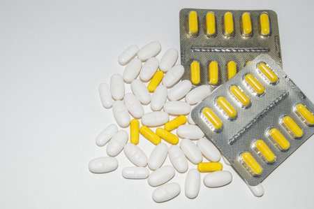 Silver blister packs of yellow pills and scattered white pills on a white background, top view, copy of spaceの写真素材