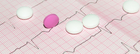 Round white and pink tablets on a paper cardiogram close-up, with a copy of the text space. Cardiac care. Concept of cardiology, medicine and insuranceの写真素材