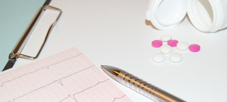 Paper cardiogram with a pen and capsules pouring out of a bottle of pills on the table, the concept of heart disease preventionの写真素材