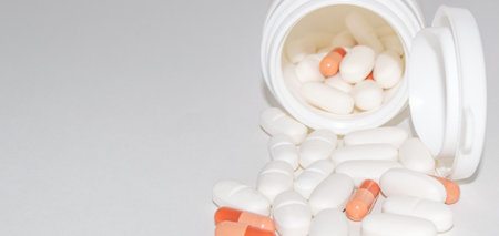 White and red pills pour out of a white plastic jar, isolated on a white background, copy of the spaceの写真素材