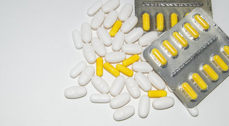 Silver blister packs of yellow pills and scattered white pills on a white background, top view, copy of spaceの写真素材