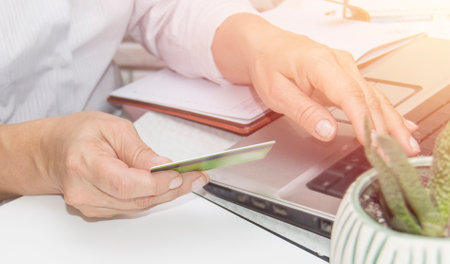 A womans hand enters data using a laptop while holding a credit card in the other hand, an online banking conceptの写真素材