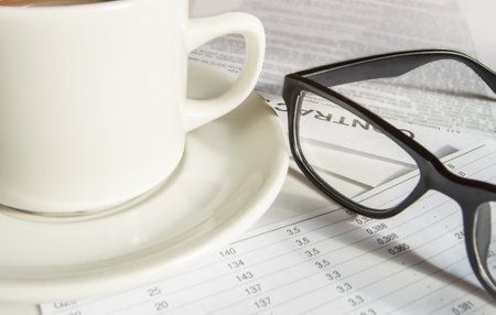 Close-up of black mens elegant glasses and a white coffee Cup standing on business papersの写真素材