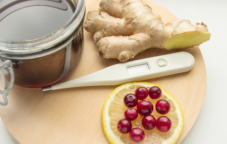 Natural cold remedies on A round WOODEN TRAY, ginger, cranberries, thermometer, jar of honey, bannerの写真素材