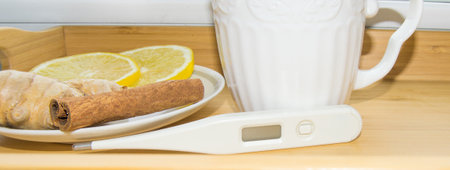 Treatment of colds and viruses, lemon, ginger, thermometer, cinnamon, tea on a wooden tray. Concept of home treatment of seasonal coldsの写真素材