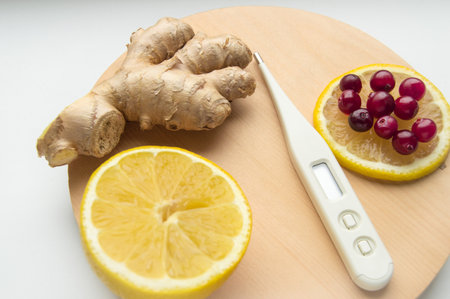 Natural cold remedies on a round WOODEN TRAY, ginger, cranberries, thermometerの写真素材
