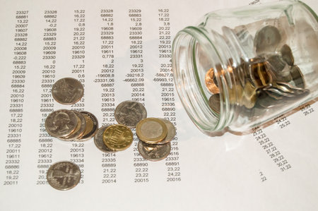 Coins spilled out of a glass jar lying on the reports with figures, the concept of investment, savings, crisisの写真素材