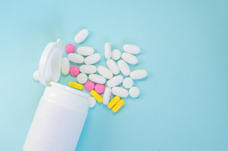 Close-up of a plastic jar with scattered pills on a blue background, the concept of medicine and pharmacyの写真素材