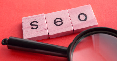 SEO search engine optimization text wooden cubes and magnifying glass on a red background. Idea,...