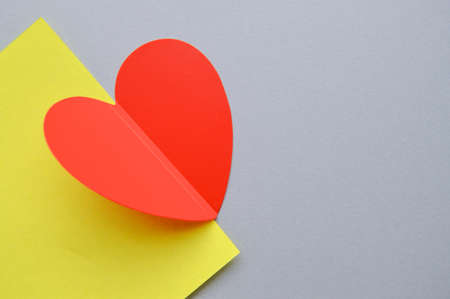 Red love heart on a piece of cut-out yellow paper and a gray background, a heart bent in halfの写真素材