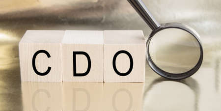 Word Business Acronym for CDO The Secured IOU consists of wood building blocks. Concept and magnifying glass on gold background with reflection, corporate bondsの写真素材