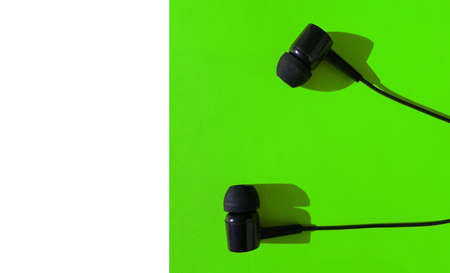 Black headphones on a green background, bright light and hard shadow, the concept of using the modern social app Clubhouse on a smartphone, white negative space on the leftの写真素材