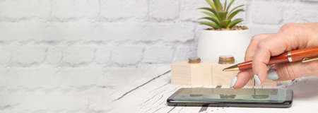 Female accountant uses a mobile phone with a pen to calculate profit and loss, business concept, office background, bannerの写真素材