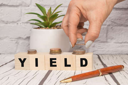 Yield a word on wooden dice and coins in your hand on a wooden table. Harvest profit business...