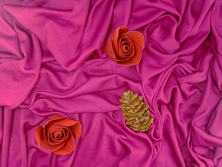 Red rose and gold pine cone on a pink satin background.