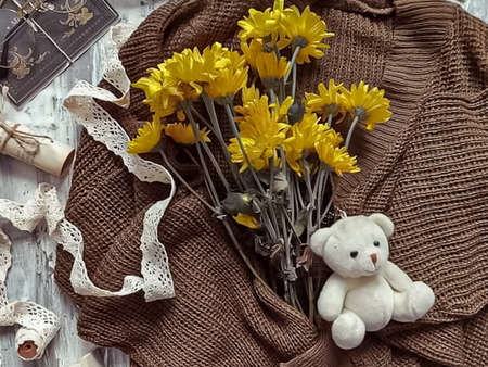 A bouquet of yellow chrysanthemums and a teddy bear on a brown knitted plaid.